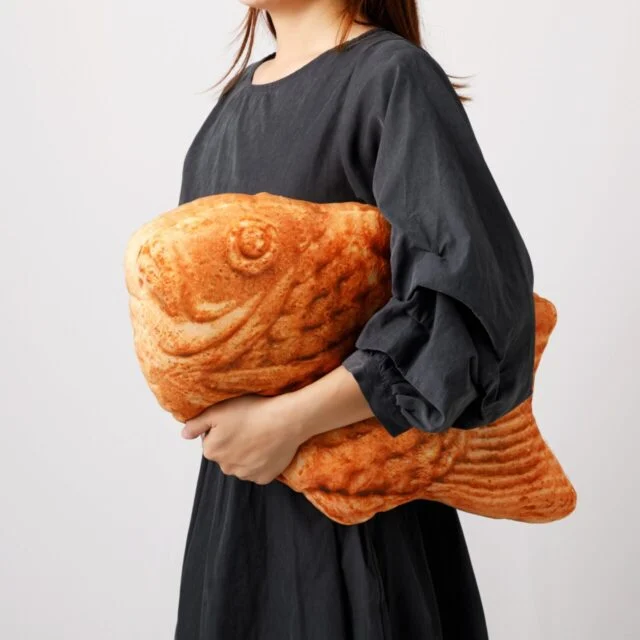 公式公表写真。鱗と魚の形を表現した、横長のたい焼き形TY001を抱える様子。